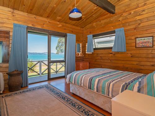 a bedroom with a bed and a large window at Norma's Place - Simpsons Beach Bach in Whitianga
