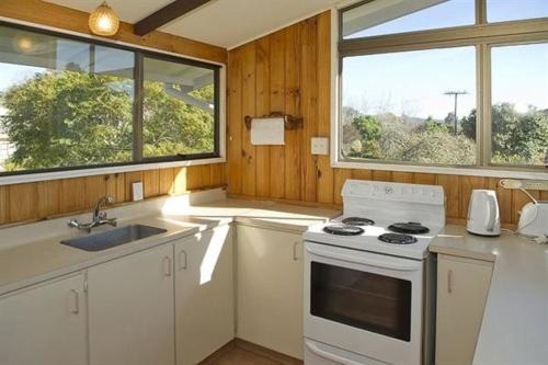 a kitchen with a stove and a sink and two windows at Joes Place - Cooks Beach Holiday Home in Cooks Beach