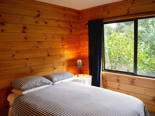 um quarto com paredes de madeira e uma cama com uma janela em Puka Lodge Front dwelling - Pukawa Bay Home em Kuratau