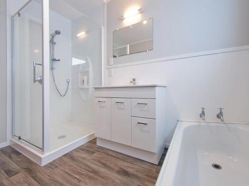 a white bathroom with a shower and a sink at Sea Breeze - Whangamata Holiday Home in Whangamata