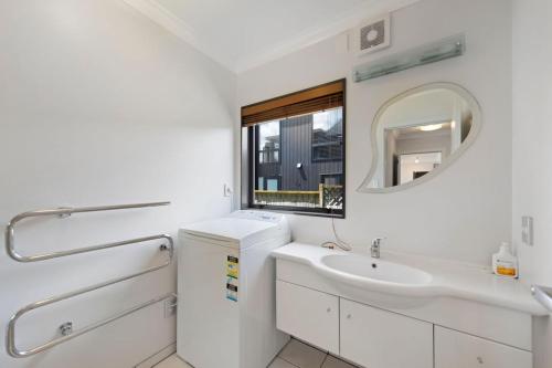 a white bathroom with a sink and a mirror at The Sandcastle - Papamoa Holiday Apartment in Papamoa