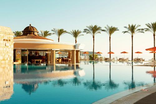 a swimming pool with palm trees and a building at Alexandra Beach Hotel in Nea Kydonia