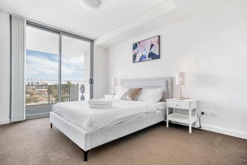 a white bedroom with a bed and a large window at KOZYGURU Parramatta Lovely 2 BED APT Free Parking NPA006 in Sydney