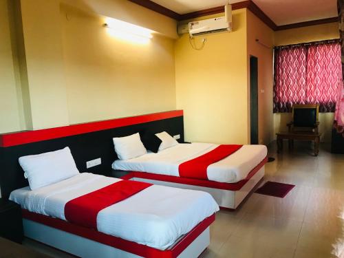 a bedroom with two beds with red and white sheets at STAYMAKER Prakash International in Gonikoppal