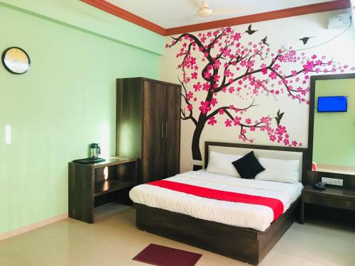 a bedroom with a bed with a tree with pink flowers at STAYMAKER Prakash International in Gonikoppal