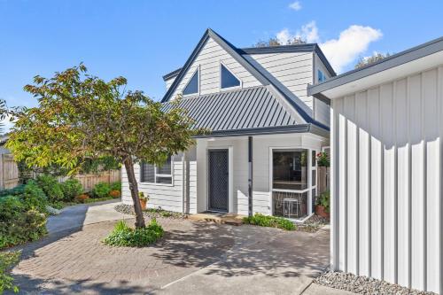 a white house with a tree in a driveway at Sandy Feet - Papamoa Beach Holiday Home in Papamoa