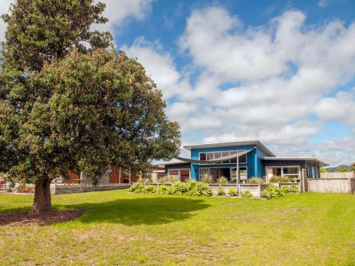 a blue house with a tree in front of it at Sands Beach House - Matarangi Holiday Home in Matarangi