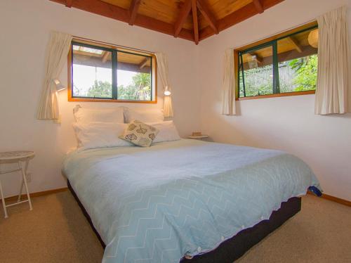 een slaapkamer met een groot bed en 2 ramen bij Cedar Cottage - Tairua Holiday Home in Tairua
