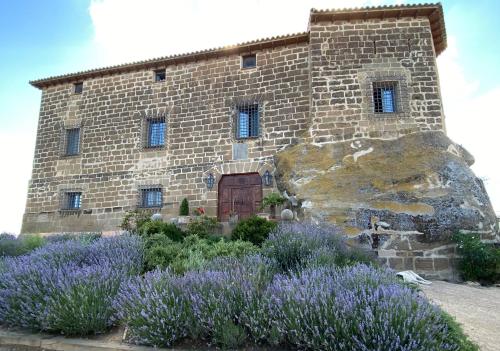 a stone building with purple flowers in front of it at Castillo de Corvinos in Huesca
