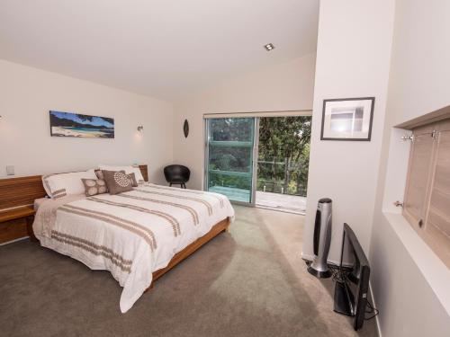 a white bedroom with a bed and a tv at Moonlit Knights - Tutukaka Holiday House in Tutukaka