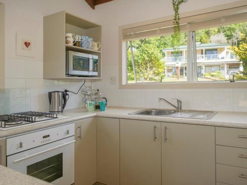a kitchen with white cabinets and a sink and a window at Oasis Tairua - Tairua Holiday Home in Tairua