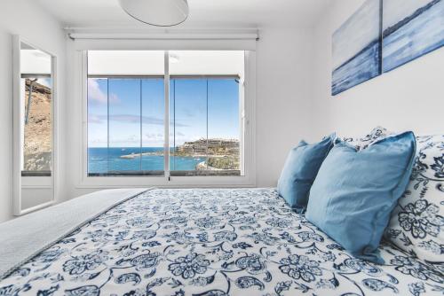 een slaapkamer met een bed en een groot raam bij Home2Book Blue Sea View Patalavaca Beach Apartment in Patalavaca