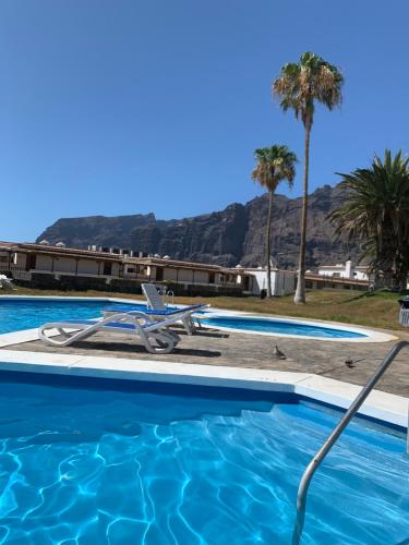 una piscina con una silla y palmeras en Ocean View, Große Sonnenterrasse, Meerblick, Tamara Komplex, Teneriffa Süd, Los Gigantes, 500m Strand, Pool, 300m zum Ort, ruhig, en Acantilado de los Gigantes