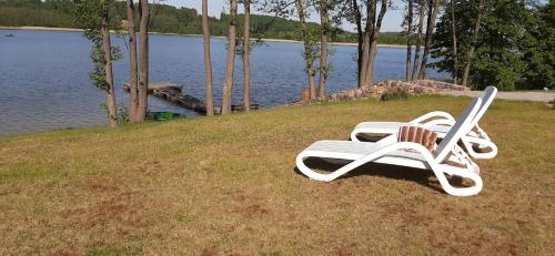a white lounge chair sitting on the grass by the water at Vila Galadusis prie ežero in Lazdijai