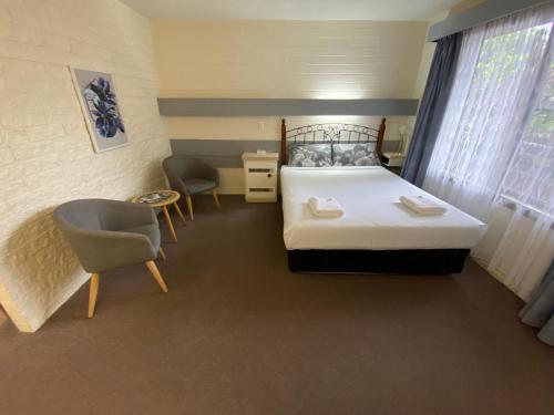 a bedroom with a bed and a chair and a table at Mahogany Motel Warrnambool in Warrnambool