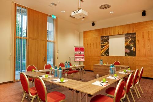a conference room with long tables and red chairs at H4 Hotel München Messe in Munich