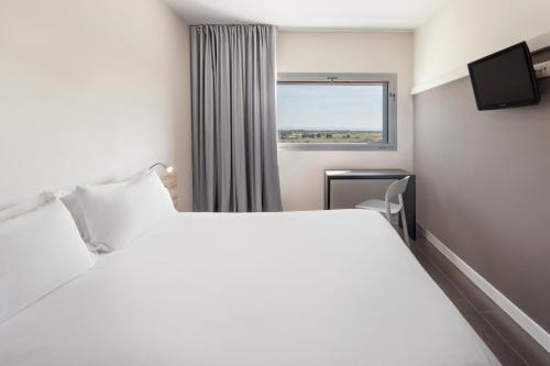 Un dormitorio con una gran cama blanca y una ventana en B&B HOTEL Albacete en Albacete