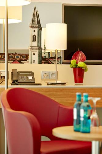 a red chair and a table with a phone and a clock tower at H4 Hotel München Messe in Munich