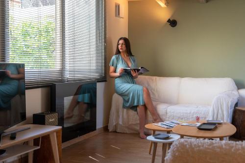 a woman sitting on a couch reading a book at Tinas Home - Kalamata Mediterranean Villas in Kalamata