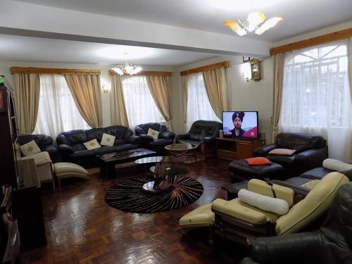 sala de estar con muebles de cuero y TV de pantalla plana en Tranquil Homestays, en Naro Moru