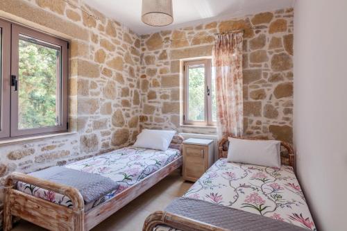 Habitación con 2 camas, paredes de piedra y ventanas. en Dream house near the beach, en Dhrapaniás