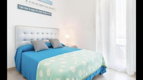 a white bedroom with a blue bed and a window at ático Tarifa in Tarifa
