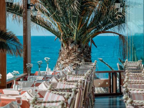 a restaurant with tables and chairs with the ocean in the background at Mitsis Cretan Village in Hersonissos