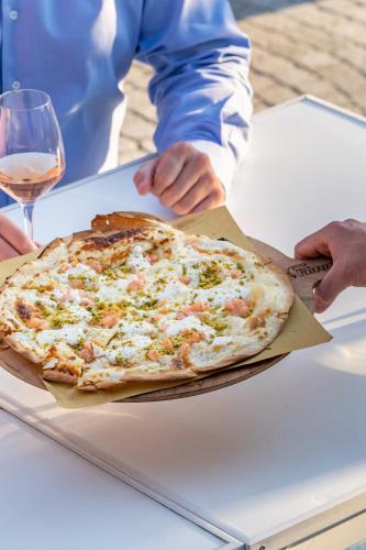 a person holding a pizza on a table with a glass of wine at Conca Bella Boutique Hotel & Wine Experience in Vacallo