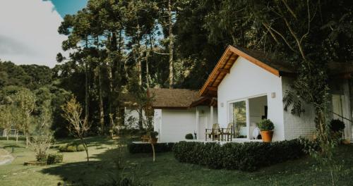 Casa blanca pequeña con porche y árboles en Roots Resort, en Monte Verde