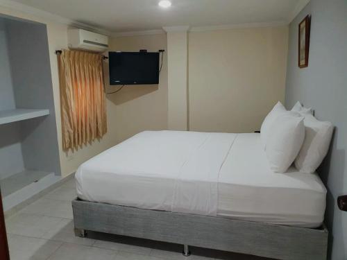 a bedroom with a white bed with a television on the wall at Hotel Puerta de Oro in Barranquilla