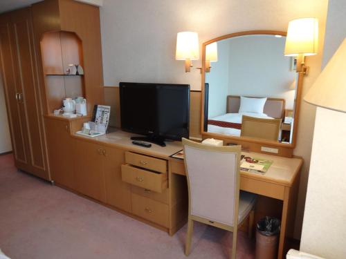 a room with a desk with a television and a bedroom at Hotel Higashinihon Utsunomiya in Utsunomiya