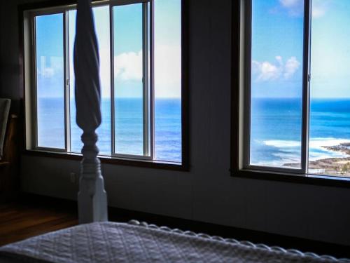 a bedroom with a view of the ocean through windows at Waimea Bay Luxury Estate Views & Hot Tub in Haleiwa