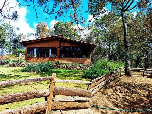 a wooden cabin in a field with a fence at Cabaña en medio del bosque ZA in Acaxochitlán