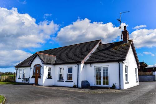 uma casa branca com um telhado preto em The Heights & Hollows Farmhouse, Saul, Downpatrick, SLEEPS 14 em Downpatrick