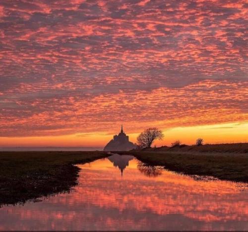 a sunset with a reflection of a building in the water at Au Mont Chez Vous #Jacuzzi et Vue Mont-St-Michel# in Huisnes-sur-Mer