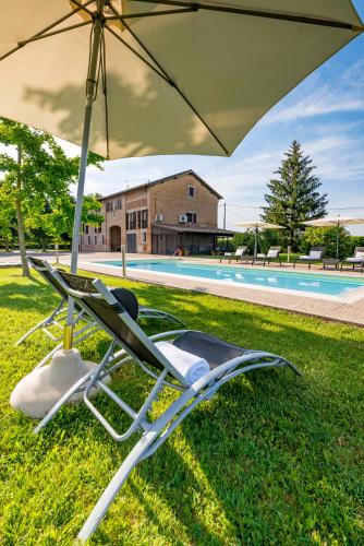 a lawn chair under an umbrella next to a pool at Casa delle Noci country house, pool & SPA in Modena