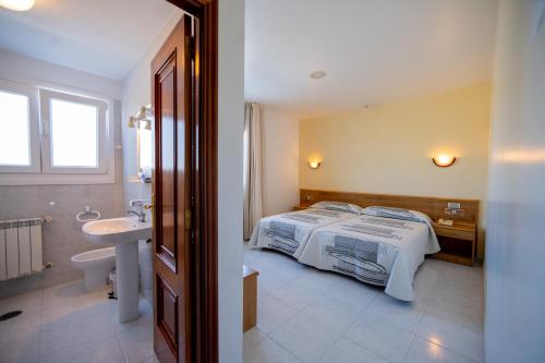a bedroom with a bed and a bathroom with a sink at Hotel Paraimo in A Lanzada