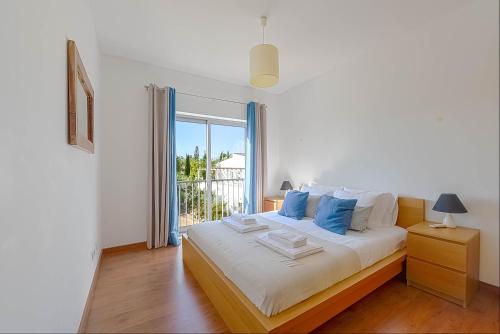een witte slaapkamer met een groot bed met blauwe kussens bij Penthouse Quilha in Fuzeta
