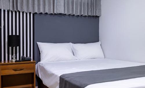 a bed with white pillows and a night stand with a lamp at Hotel Taurus in Piura