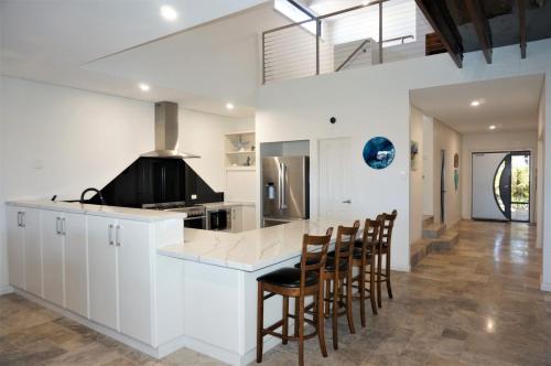 a kitchen with white cabinets and a bar with chairs at 27 Corella Court in Exmouth