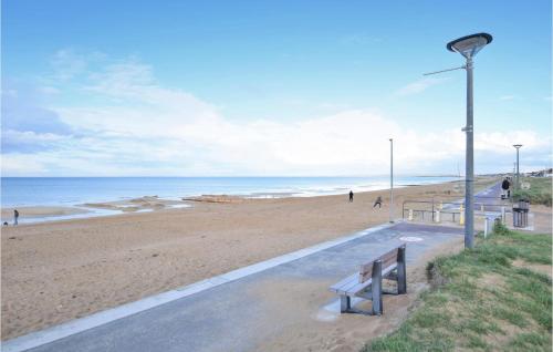 a beach with a bench and people walking on the beach at Amazing Home In Hermanville-Sur-Mer in Hermanville-sur-Mer