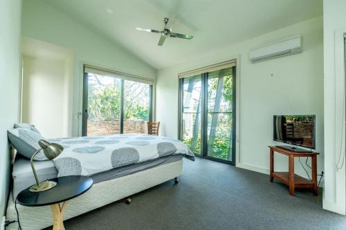 a bedroom with a bed and a tv and windows at Serenity by the Sea Inverloch in Inverloch