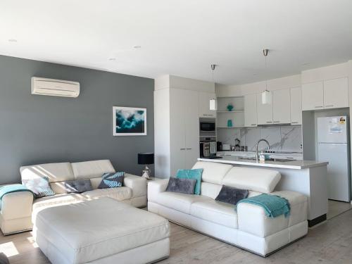 a living room with two white couches and a kitchen at At Broadbeach Inverloch in Inverloch