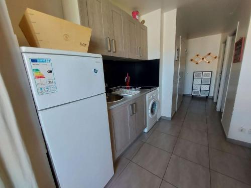 La cuisine est équipée d'un réfrigérateur blanc et d'un lave-vaisselle. dans l'établissement Appartement climatisé pour 4 à 200m de la plage, au cœur de Marseillan-Plage - FR-1-326-769, à Marseillan