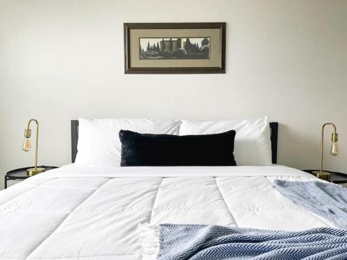 a white bed with a black pillow and two lamps at Sleepover Downtown Cincinnati 1BD 1BA Apartments in Cincinnati