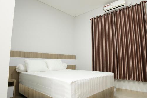 a bedroom with a white bed and a brown curtain at Djuragan Kamar Griya Permata in Ngemplak