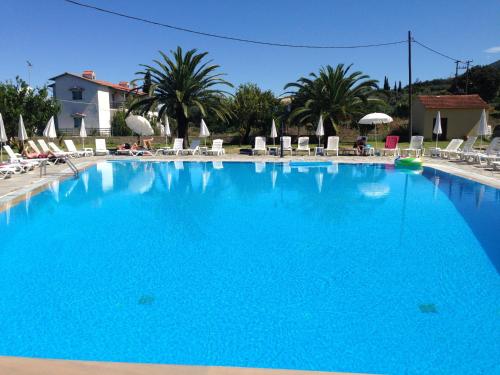 a large blue swimming pool with chairs and palm trees at Tzilios Studios in Acharavi