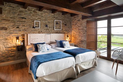 two beds in a room with a stone wall at Hotel Rural La Sobreisla in Puerto de Vega