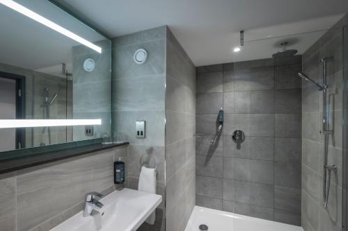 a bathroom with a shower, sink, and mirror at Maldron Hotel Manchester City Centre in Manchester