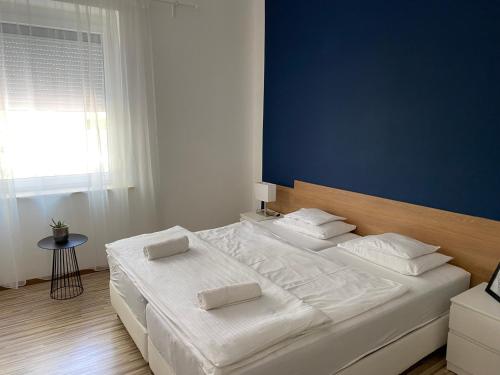 a bedroom with a large white bed with a blue wall at Élmény Balaton Hotel in Alsóörs